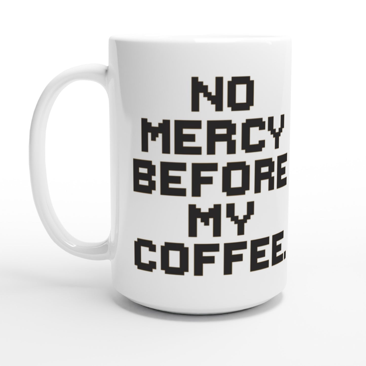 Taza friki No Mercy Before My Coffee 440 ml colocada en escritorio gamer, diseño retro para fans del pixel art y el café matutino.